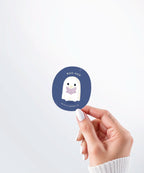 Hand holding a Nuts & Lemons Co. diecut sticker featuring a cute ghostie  reading a glowing book with the phrase “boo -ked”