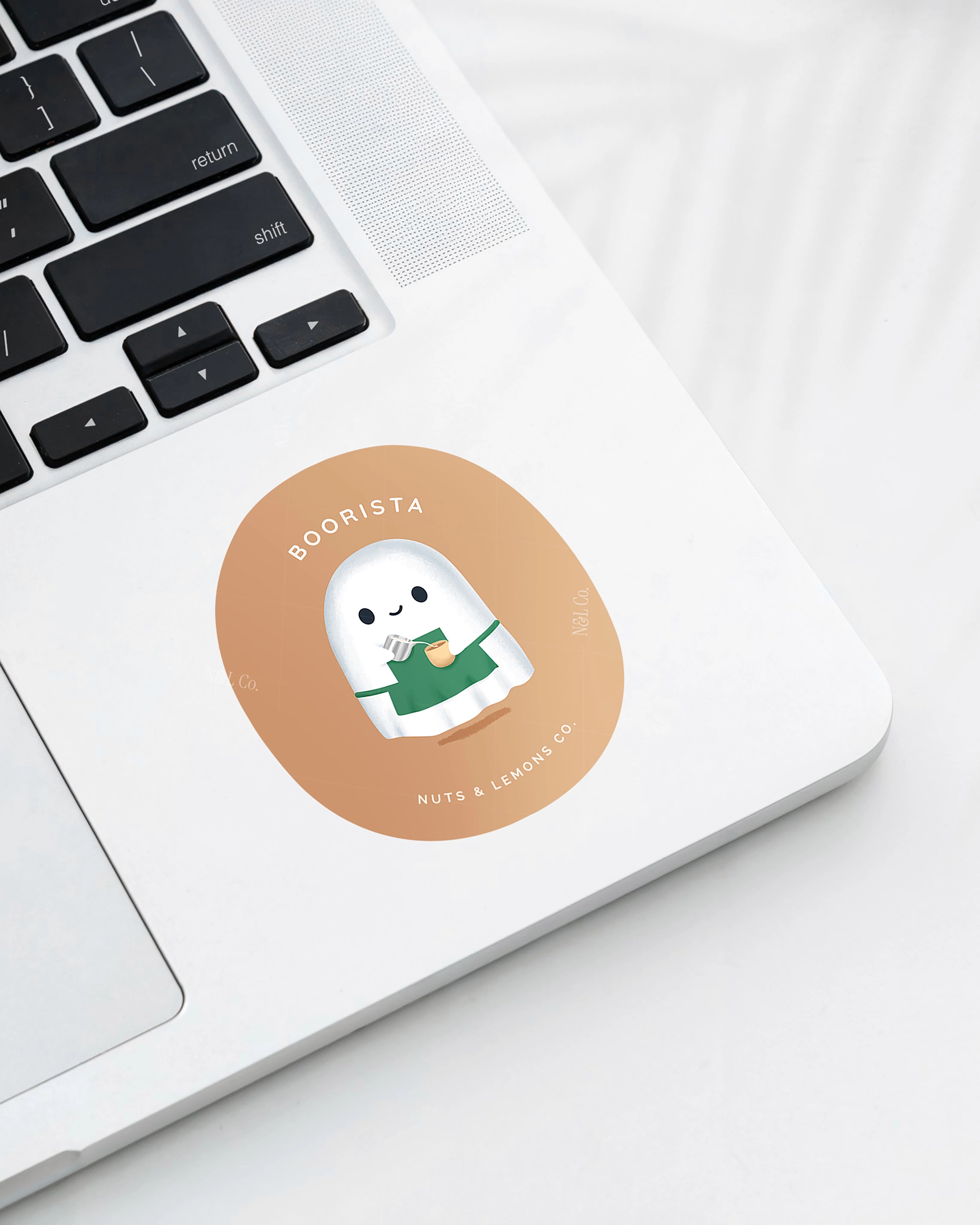Laptop displaying a Nuts & Lemons Co. diecut sticker featuring  a cute ghostie barista making a latte with the phrase “boorista”