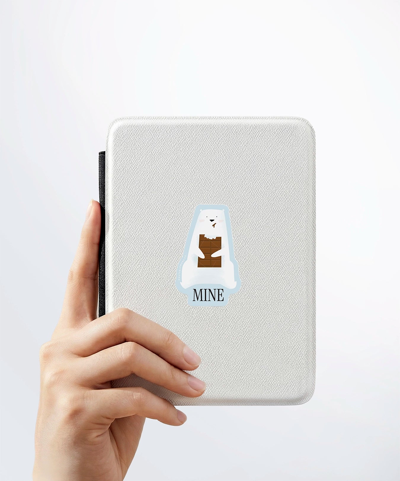A hand holding a white kindle cover with a Nuts & Lemons Co. diecut sticker on it featuring a polar bear chomping a brick of chocolate with the phrase “Miner”