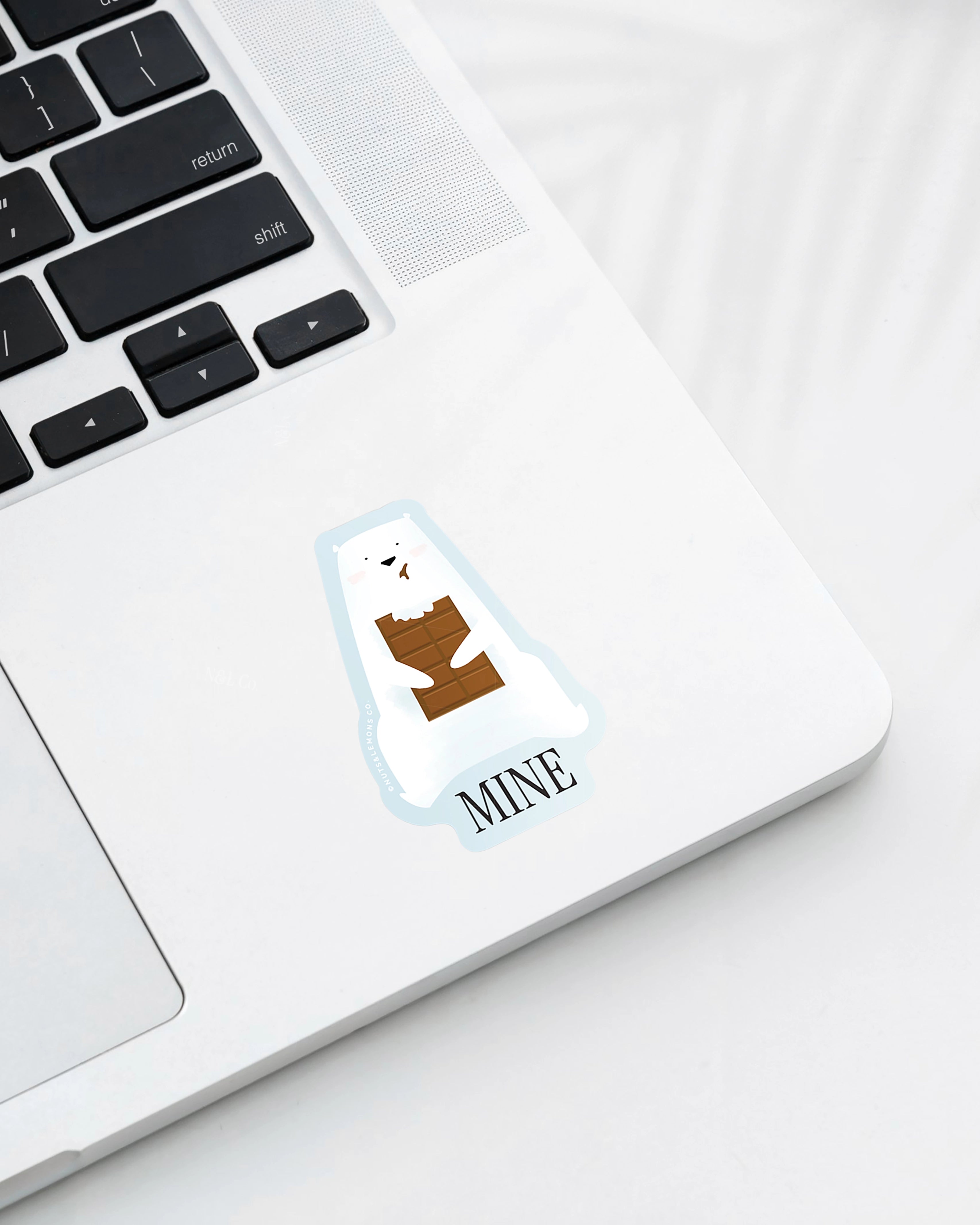 Laptop displaying a Nuts & Lemons Co. diecut sticker featuring a polar bear chomping a brick of chocolate with the phrase “mine”