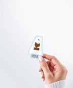 Hand holding a Nuts & Lemons Co. diecut sticker featuring a polar bear chomping a brick of chocolate with the phrase “mine”