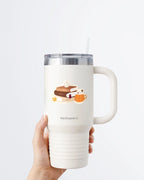 Hand holding a tumbler displaying Nuts & Lemons Co. diecut sticker featuring a stack of autumnal books, candle and psl with the phrase “cozy season and chapters”