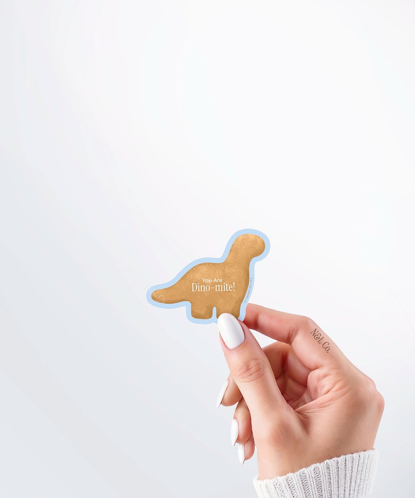 Hand holding a Nuts & Lemons Co. diecut sticker featuring a Dino nug with the phrase “you are Dino-mite”