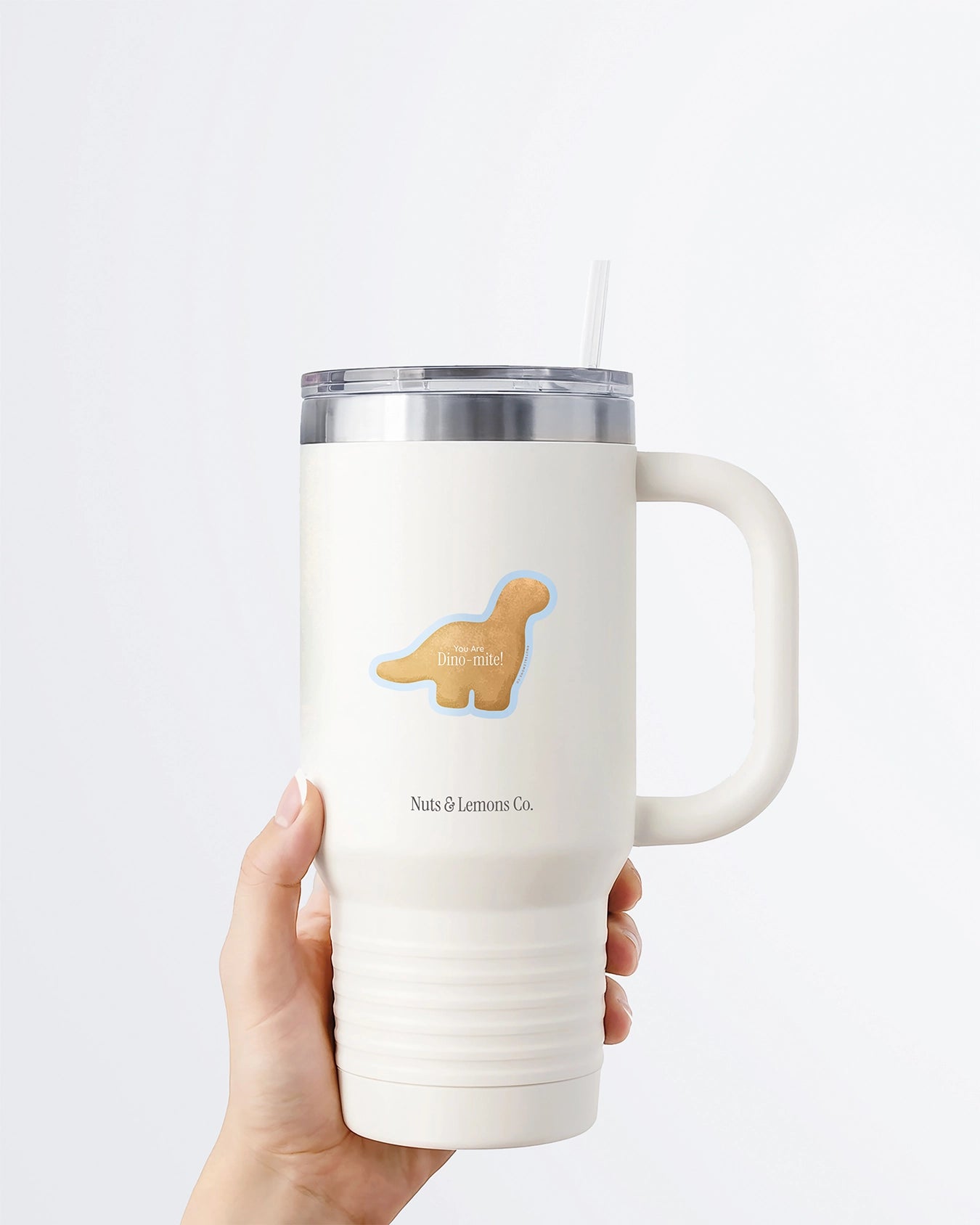Hand holding a tumbler displaying a Nuts & Lemons Co. diecut sticker featuring a Dino nug with the phrase “you are Dino-mite”