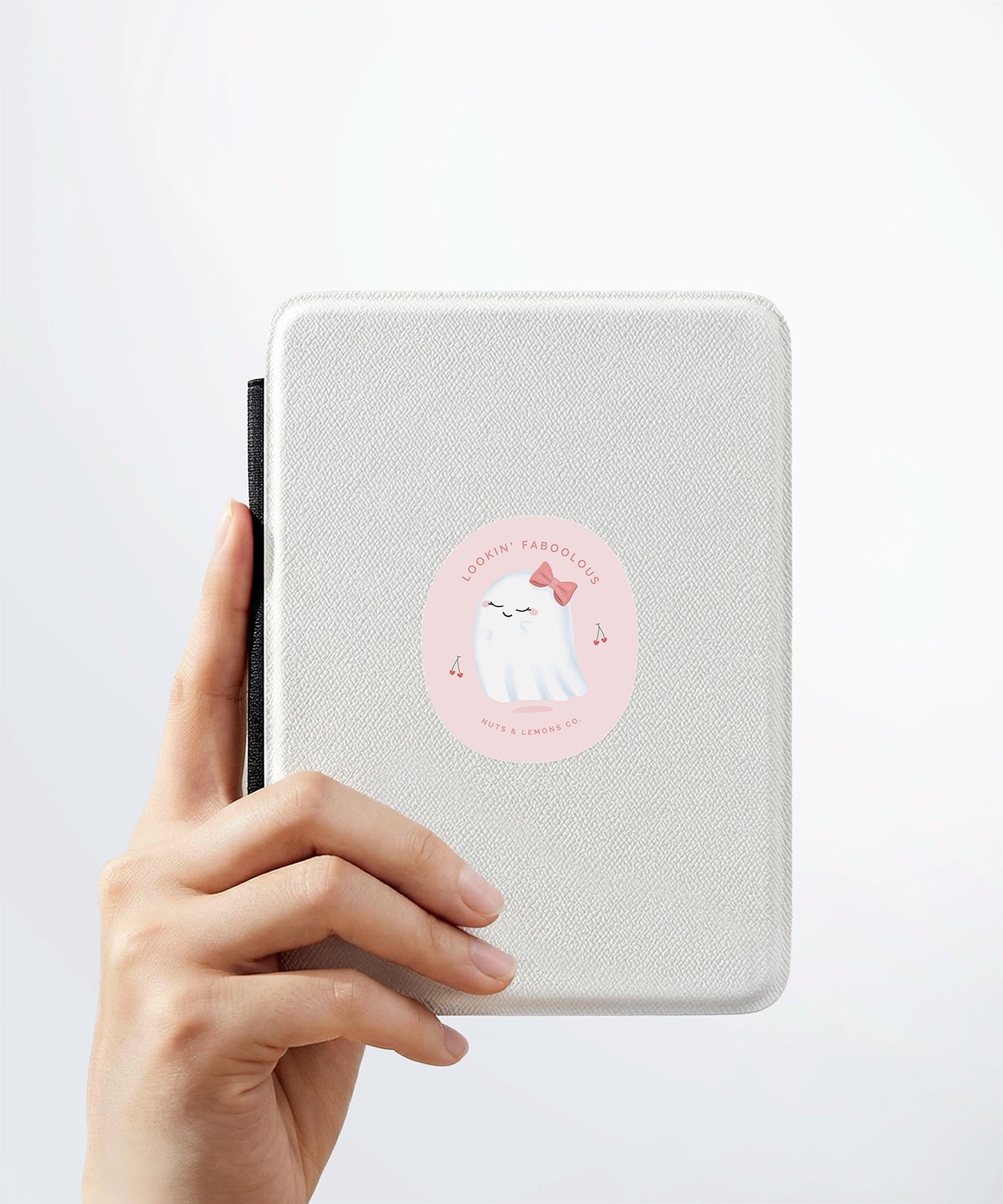 A hand holding a white kindle cover with a Nuts & Lemons Co. diecut sticker on it featuring a calm shiitake mushroom with the phrase “Let That Shittake Go”