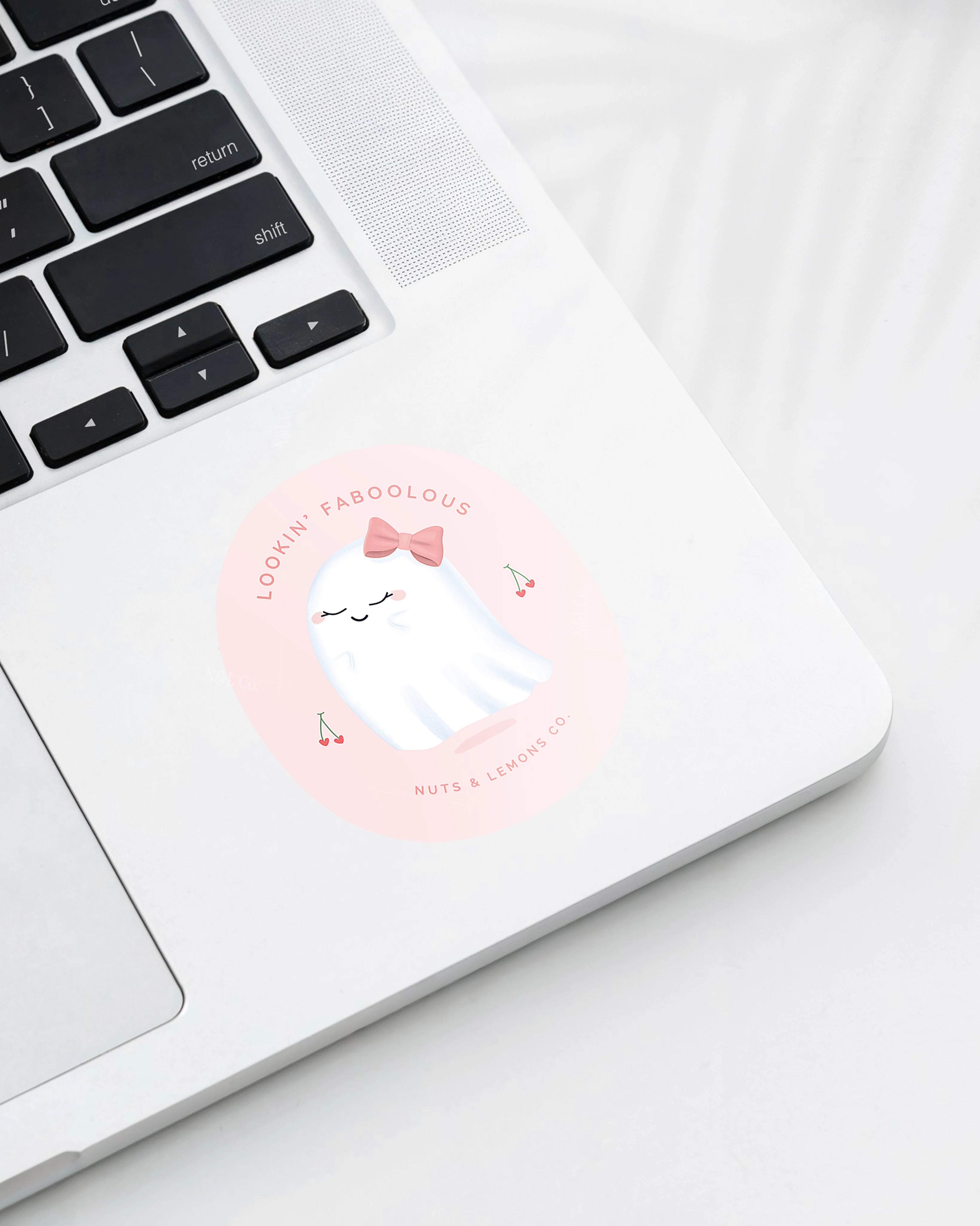 Laptop displaying a Nuts & Lemons Co. diecut sticker featuring a cute ghostie with a pink bow surrounded by heart cherries with the phrase “lookin’ faboolous”