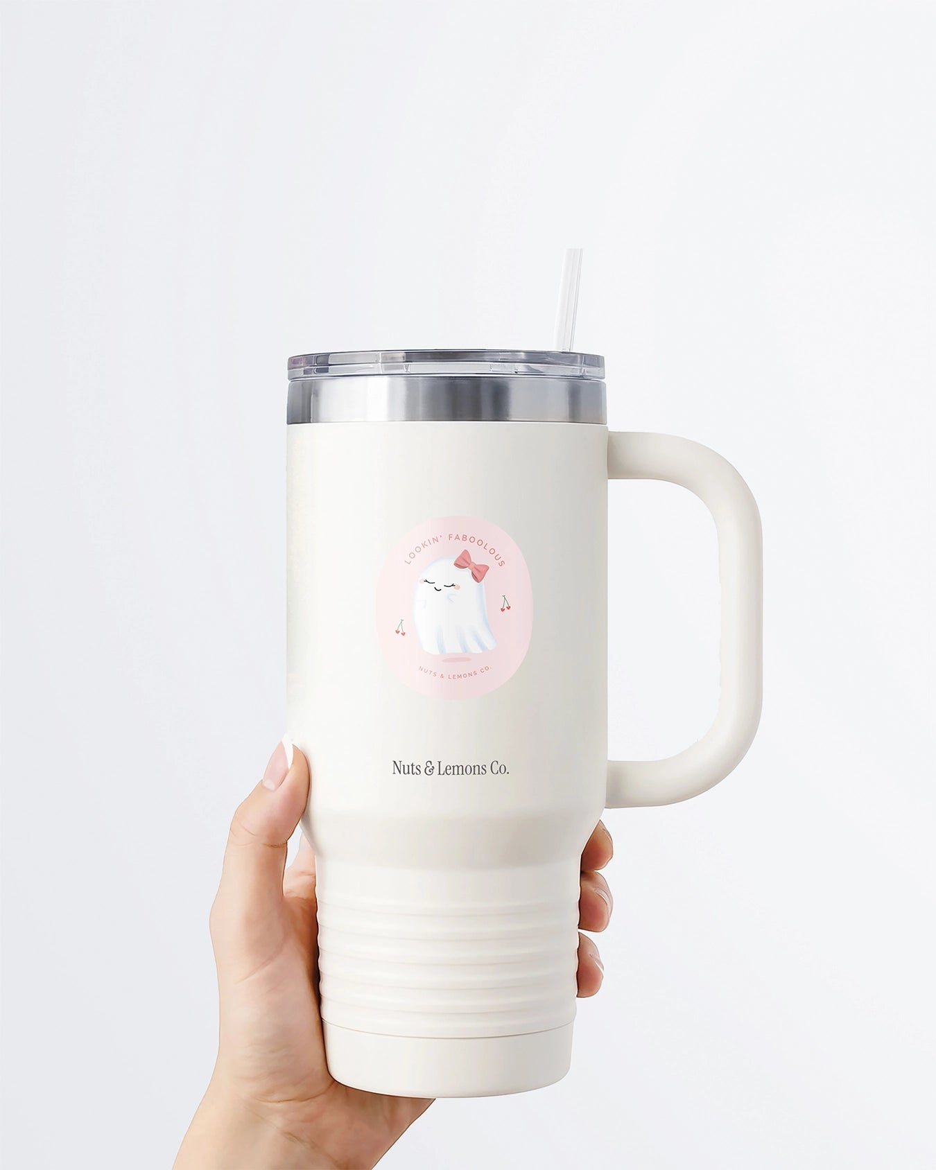 Hand holding a tumbler displaying Nuts & Lemons Co. diecut sticker featuring a cute ghostie with a pink bow surrounded by heart cherries with the phrase “lookin’ faboolous”