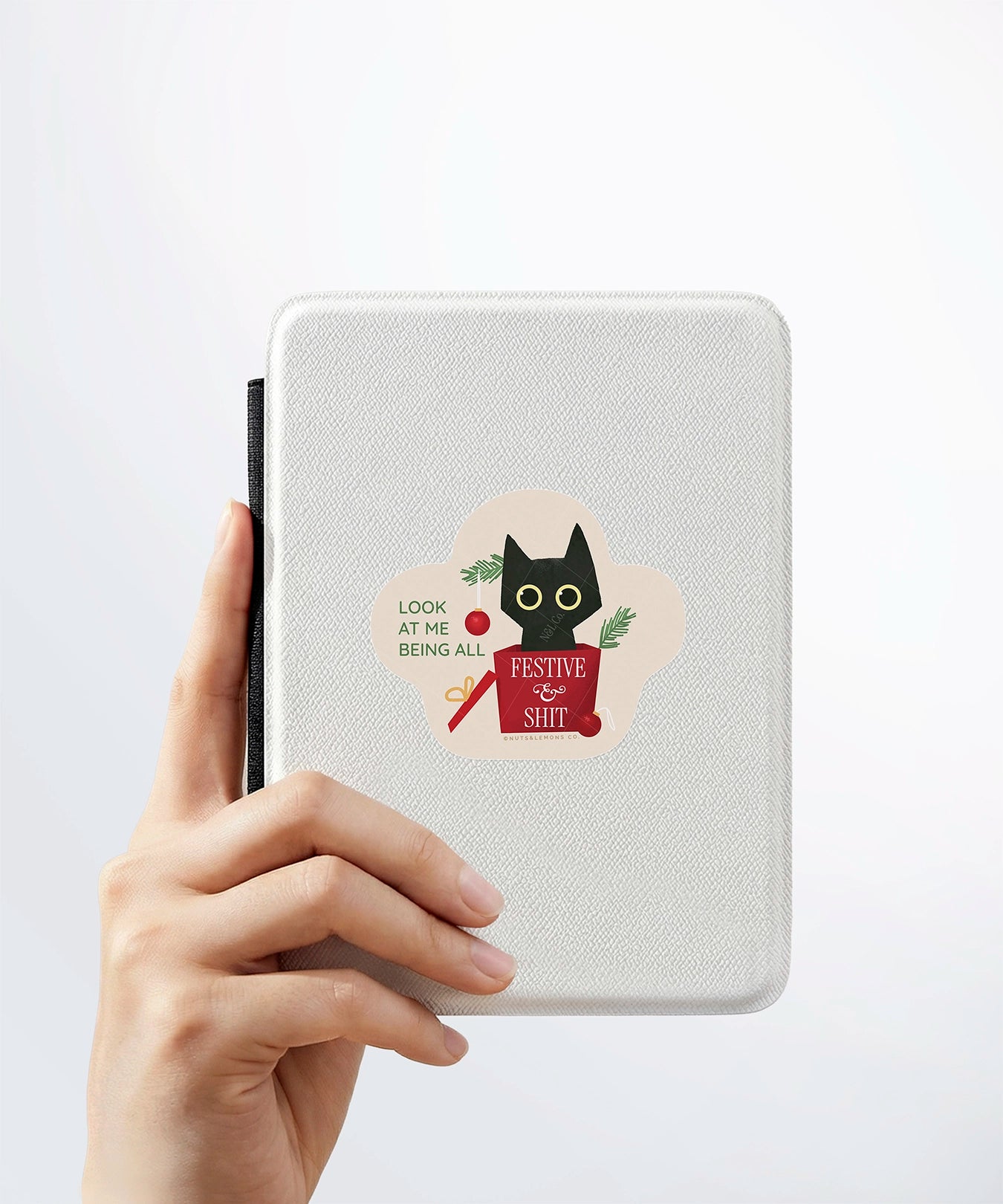 A hand holding a white kindle cover with a Nuts & Lemons Co. diecut sticker on it featuring a calm shiitake mushroom with the phrase “Let That Shittake Go”