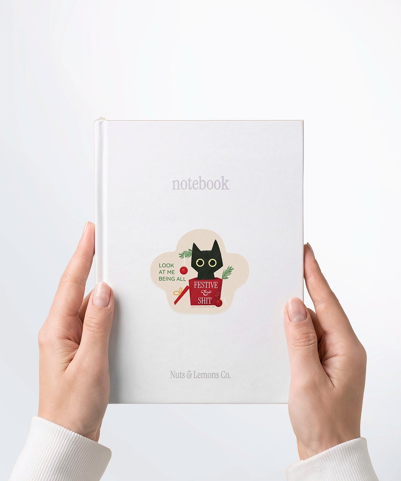 A pair of hands holding a white notebook with a Nuts & Lemons Co. diecut sticker on it featuring a calm shiitake mushroom with the phrase “Let That Shittake Go”