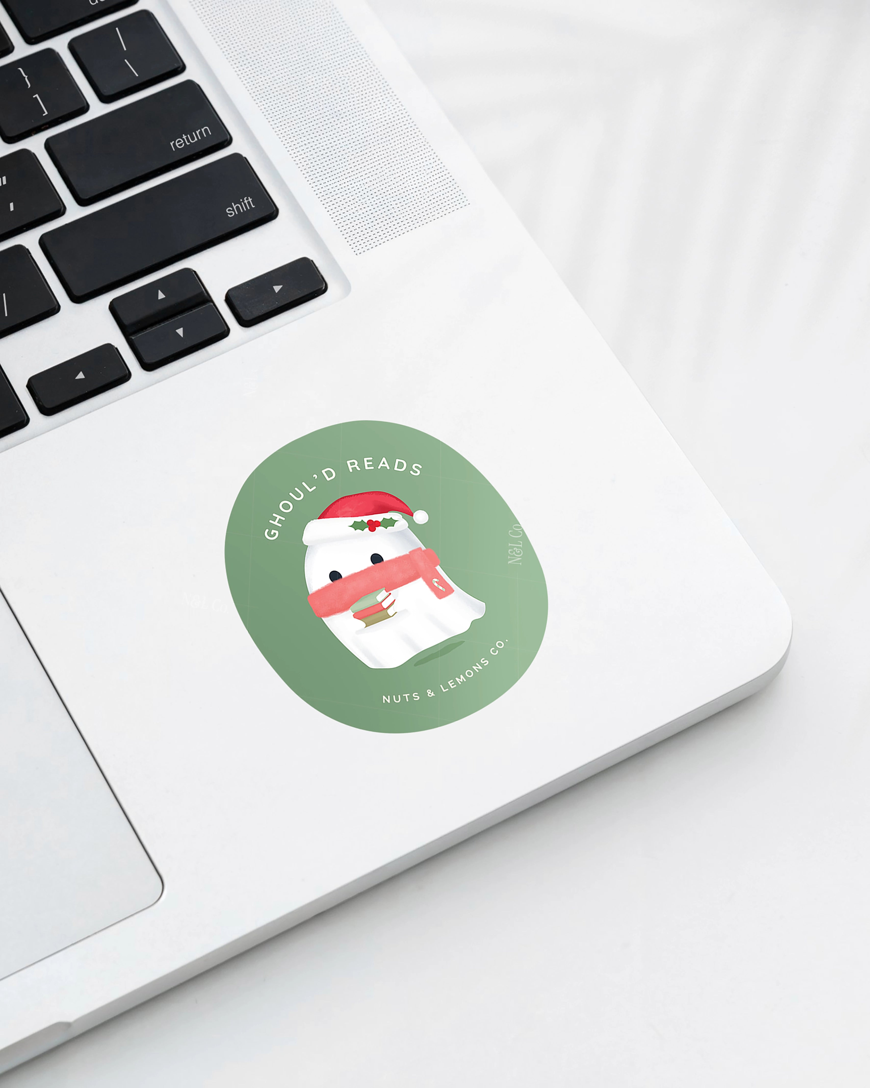 Laptop displaying a Nuts & Lemons Co. diecut sticker featuring a cute ghostie with books, Santa hat and scarf  with the phrase “ghoul’d reads”