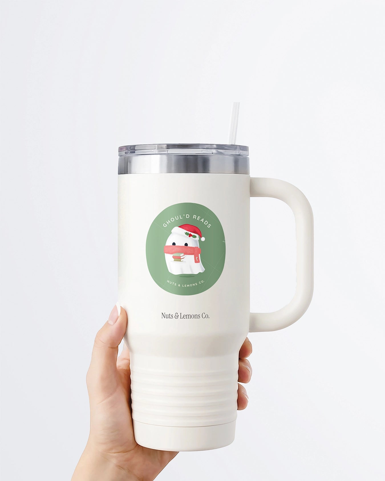 Hand holding a tumbler displaying Nuts & Lemons Co. diecut sticker featuring a cute ghostie with books, Santa hat and scarf  with the phrase “ghoul’d reads”