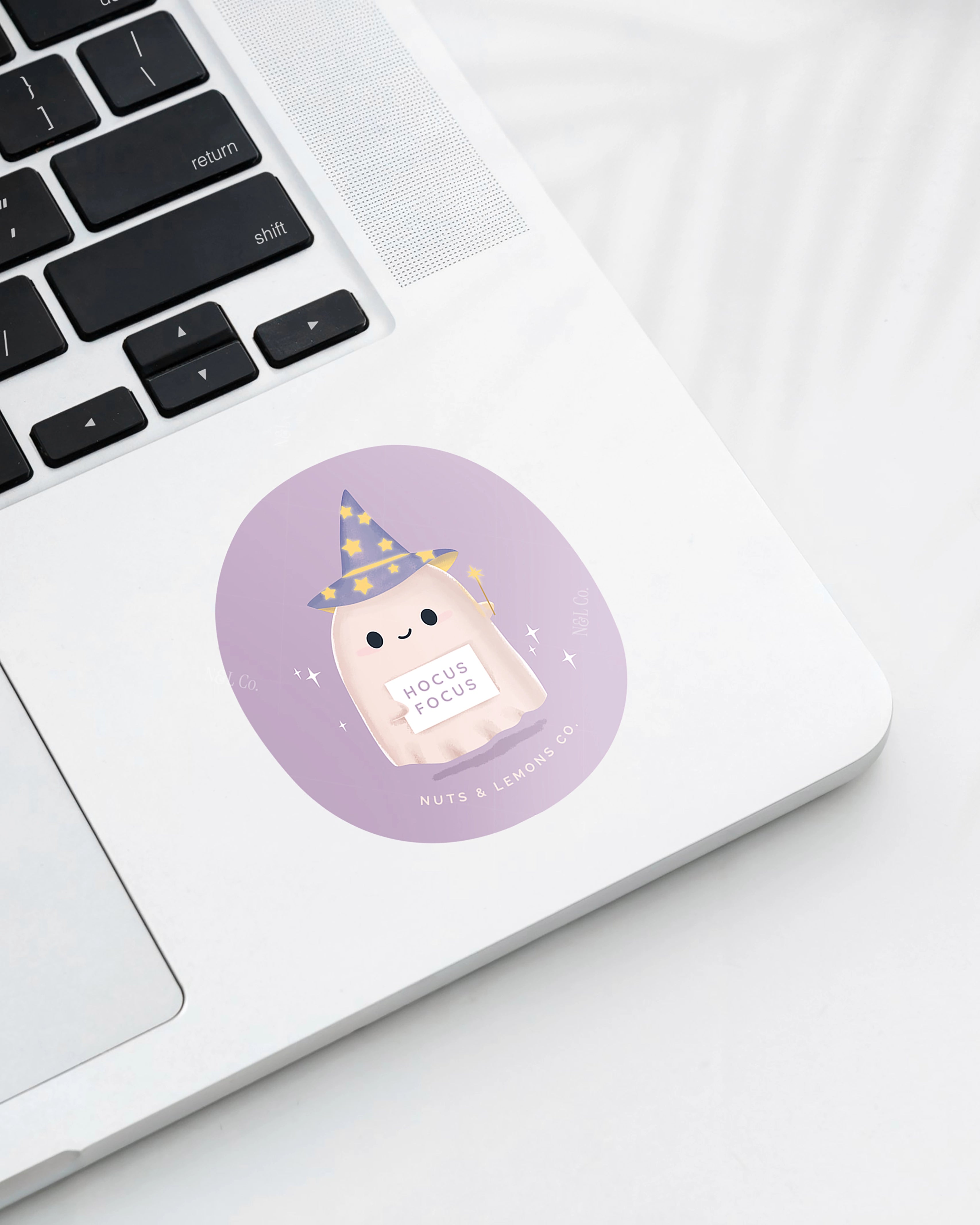 Laptop displaying a Nuts & Lemons Co. diecut sticker featuring a cute ghostie wearing a starry wizard hat, a magic wand  and a sign with the phrase “hocus focus"