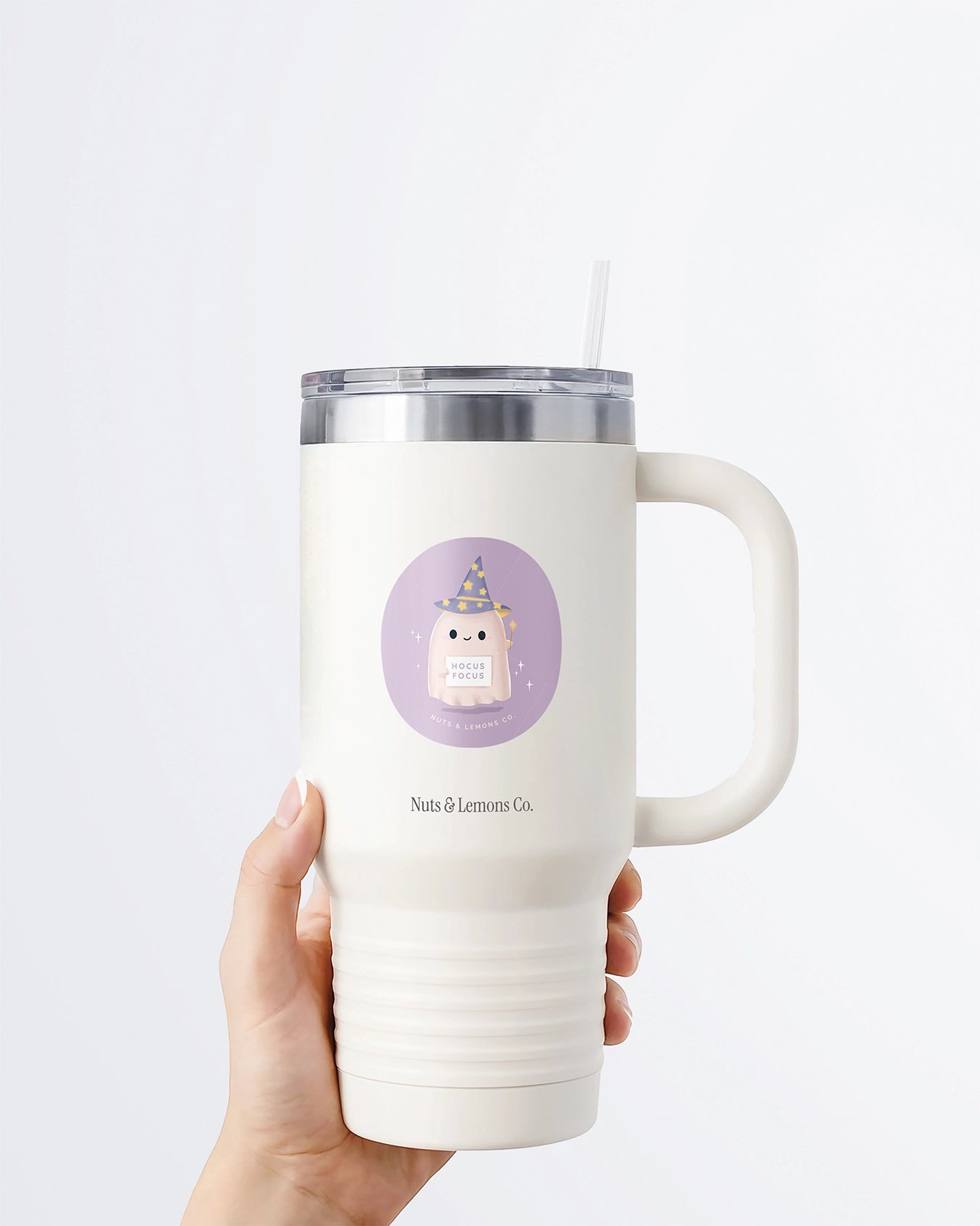 Hand holding a tumbler displaying Nuts & Lemons Co. diecut sticker featuring a cute ghostie wearing a starry wizard hat, a magic wand  and a sign with the phrase “hocus focus”