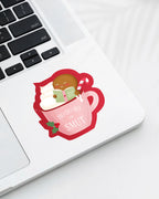 Laptop displaying a Nuts & Lemons Co. diecut sticker featuring a blushing gingerbread reading a spicy book while holding a candy cane hot tubbing in a pink mug with the phrase 
