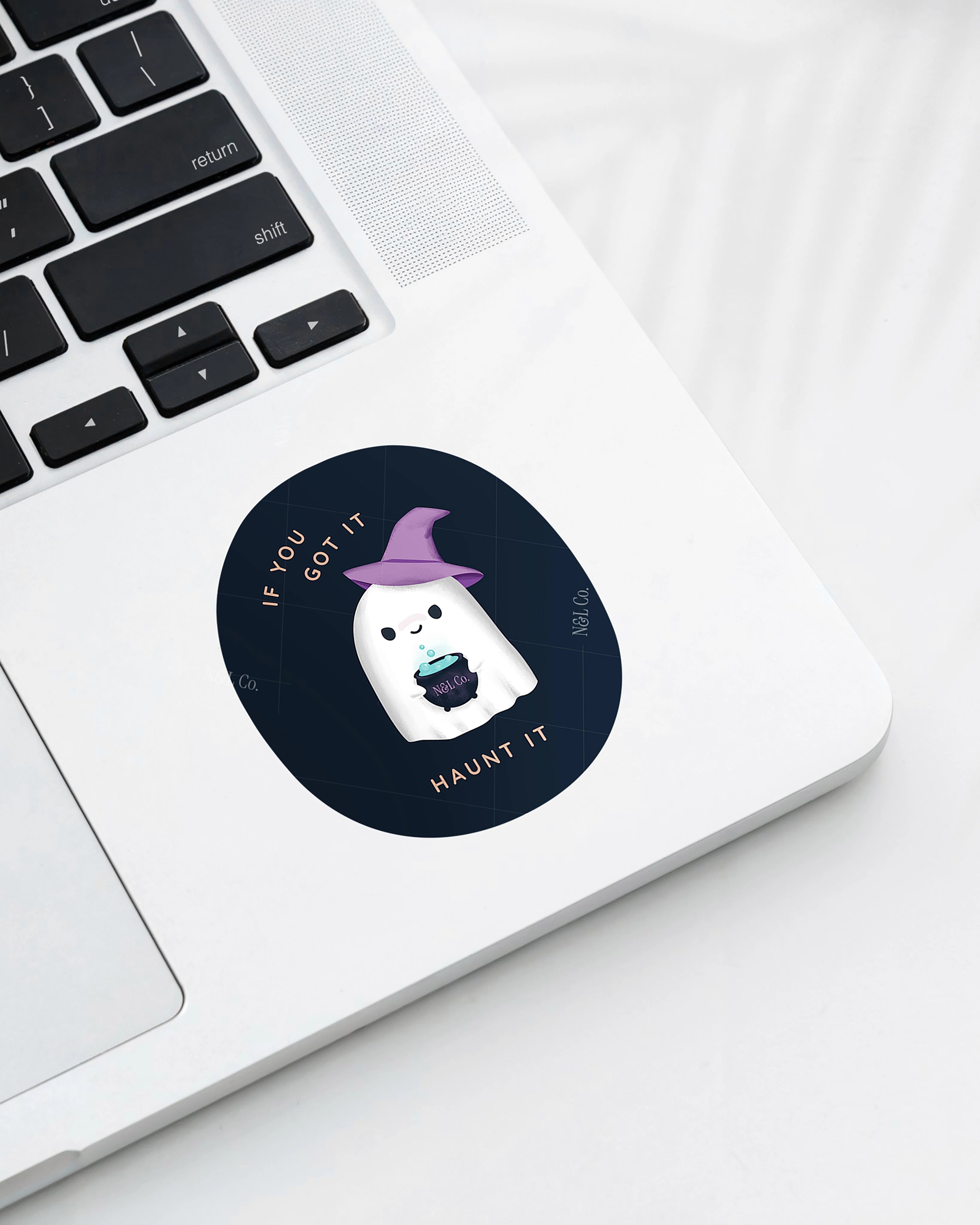 Laptop displaying a Nuts & Lemons Co. diecut sticker featuring a cute ghostie in a witch hat with a bubbling cauldron with the phrase “if you got it, haunt it”