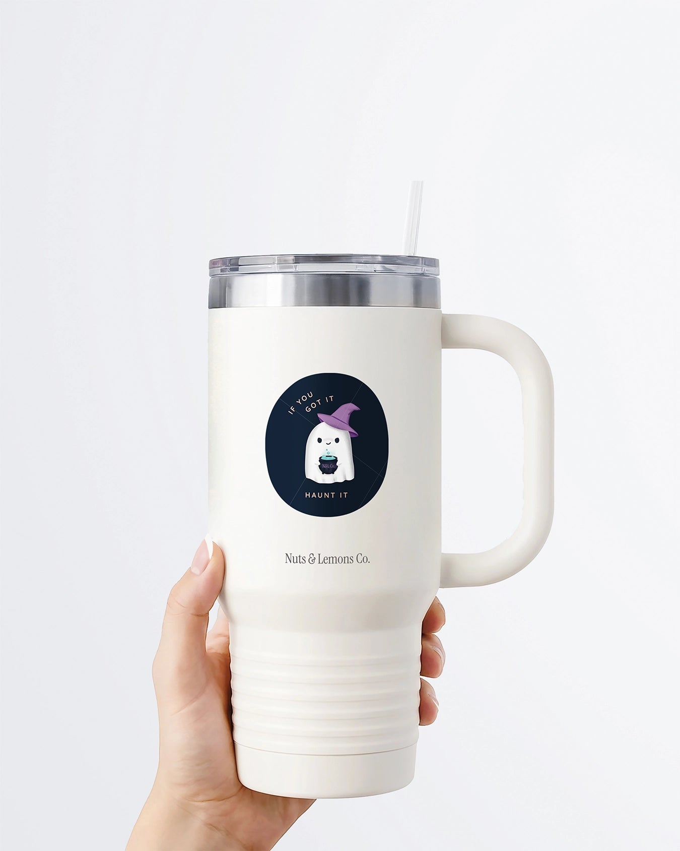 Hand holding a tumbler displaying Nuts & Lemons Co. diecut sticker featuring a cute ghostie in a witch hat with a bubbling cauldron with the phrase “if you got it, haunt it”
