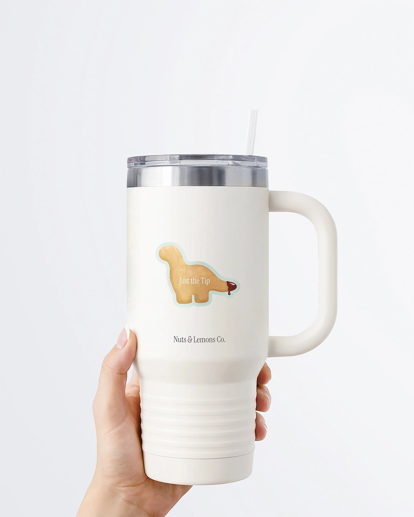 Hand holding a tumbler displaying a Nuts & Lemons Co. diecut sticker featuring a Dino nug with tail dipped in sauce with the phrase “just the tip”