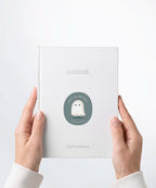 A pair of hands holding a white notebook with a Nuts & Lemons Co. diecut sticker on it featuring a cute annoyed ghostie with the phrase “Keep the Boo-Sheet”