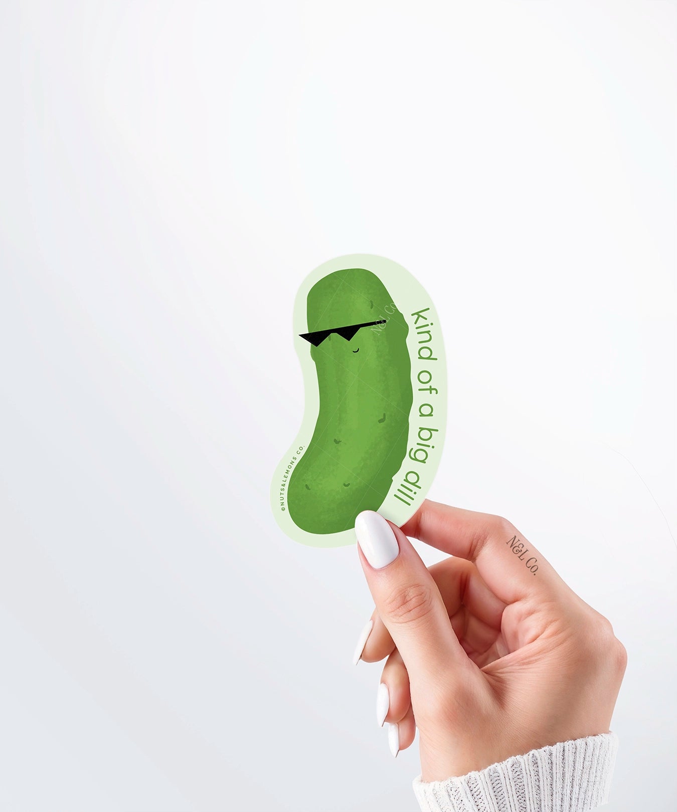 Hand holding a Nuts & Lemons Co. diecut sticker featuring a dill pickle with shades with the phrase “kind of a big dill”