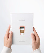A pair of hands holding a white notebook with a Nuts & Lemons Co. diecut sticker on it featuring a togo coffee with the phrase with the phrase “Love Yourself as Much as You Love Coffee”