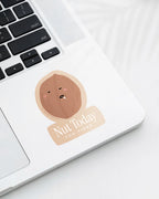 Laptop displaying a Nuts & Lemons Co. diecut sticker featuring a walnut drooling asleep with the phrase “nut today too tired”
