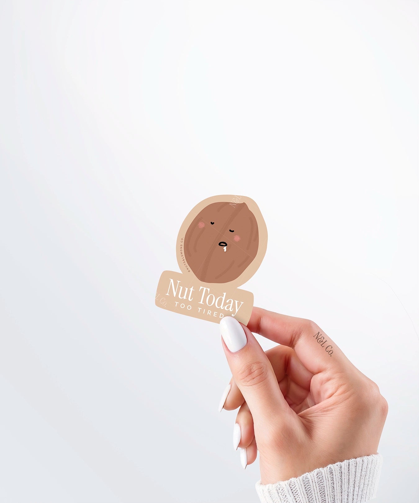 Hand holding a Nuts & Lemons Co. diecut sticker featuring a walnut drooling asleep with the phrase “nut today too tired”
