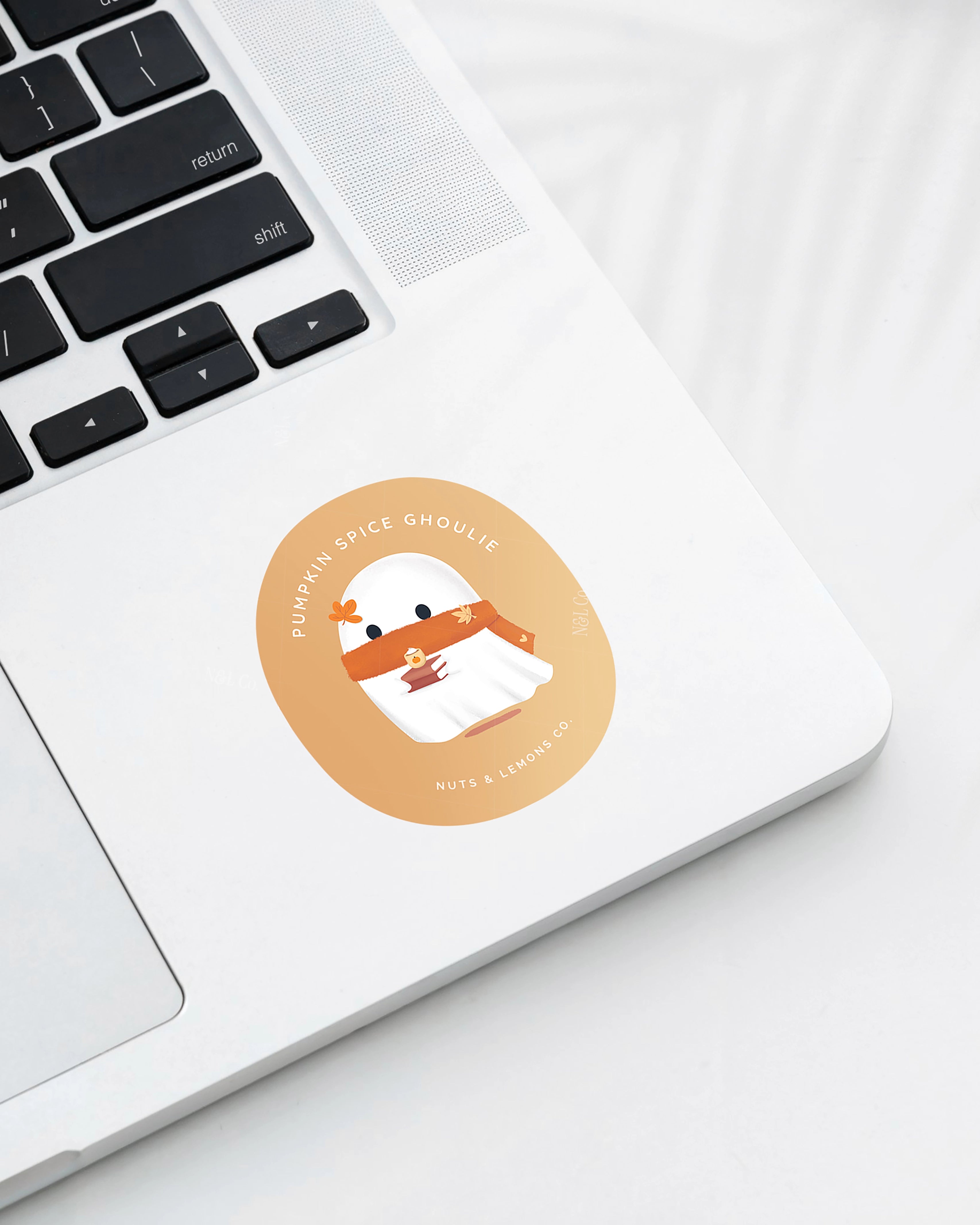 Laptop displaying a Nuts & Lemons Co. diecut sticker featuring a cute ghostie with autumn books, scarf and psl with the phrase “pumpkin spice ghoulie”