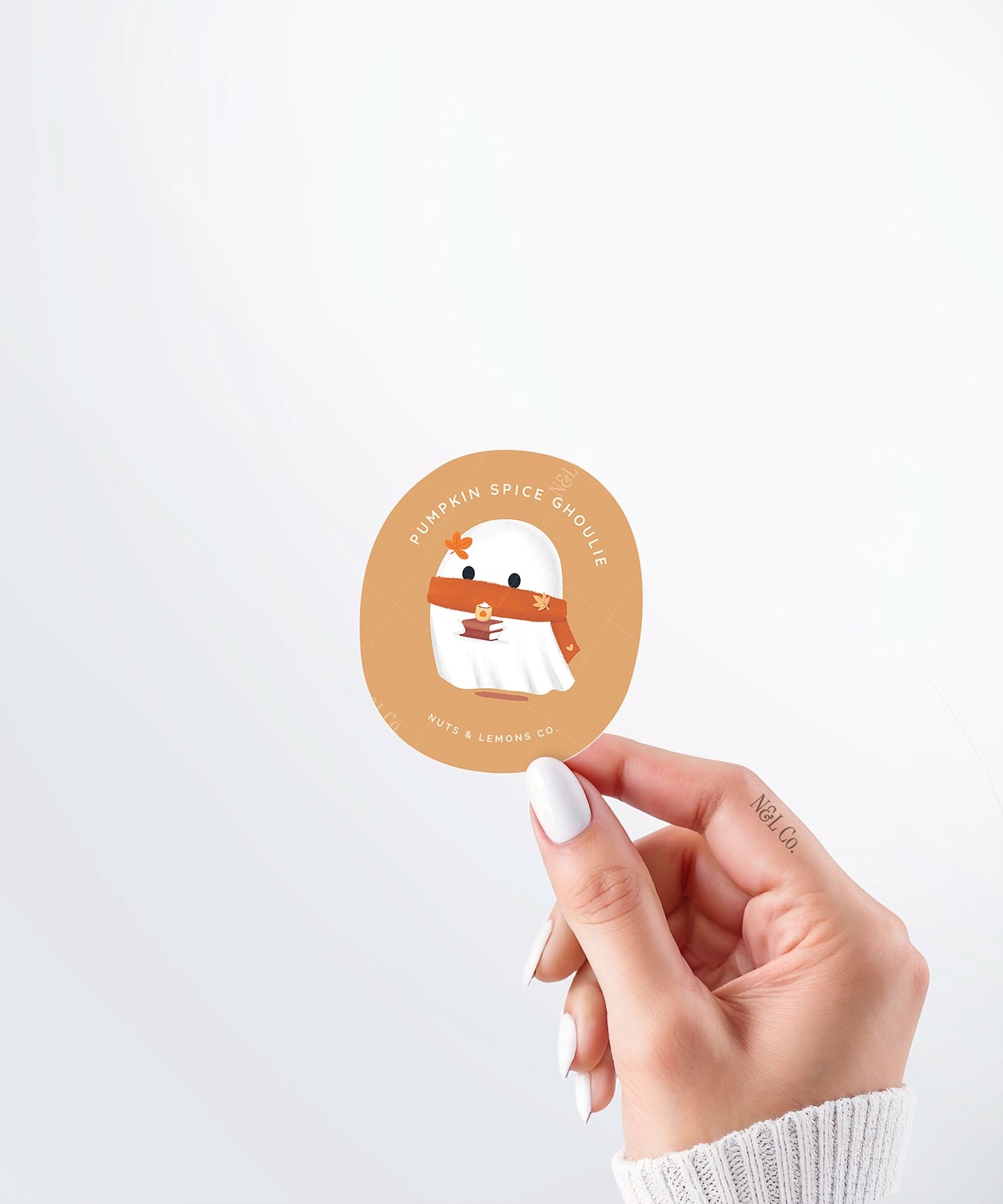 Hand holding a Nuts & Lemons Co. diecut sticker featuring a cute ghostie with autumn books, scarf and psl with the phrase “pumpkin spice ghoulie”