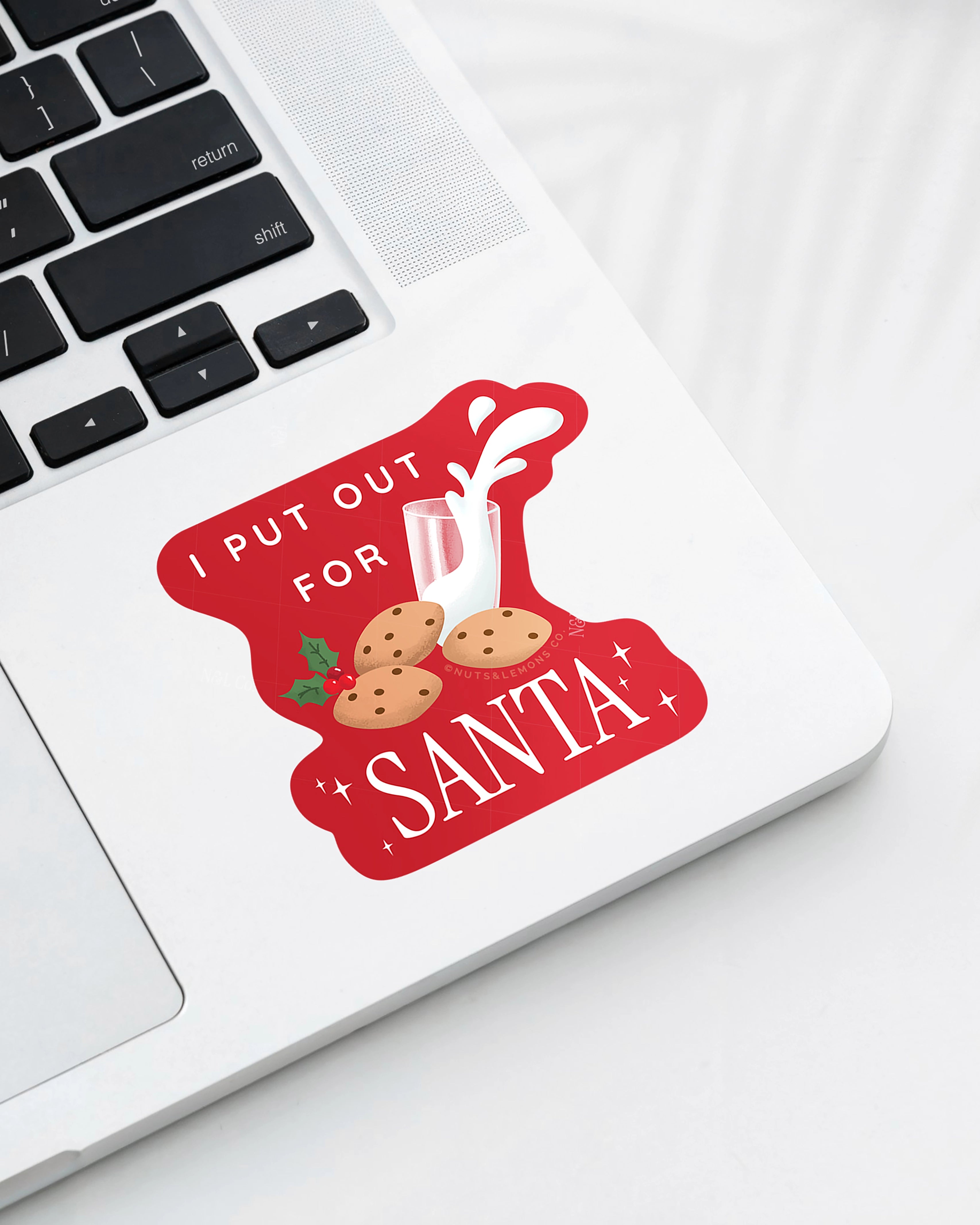 Laptop displaying a Nuts & Lemons Co. diecut sticker featuring a bunch of cookies and spilling milk with the phrase “I put out for Santa”
