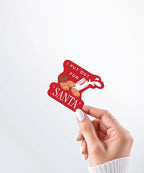 Hand holding a Nuts & Lemons Co. diecut sticker featuring a bunch of cookies and spilling milk with the phrase “I put out for Santa”
