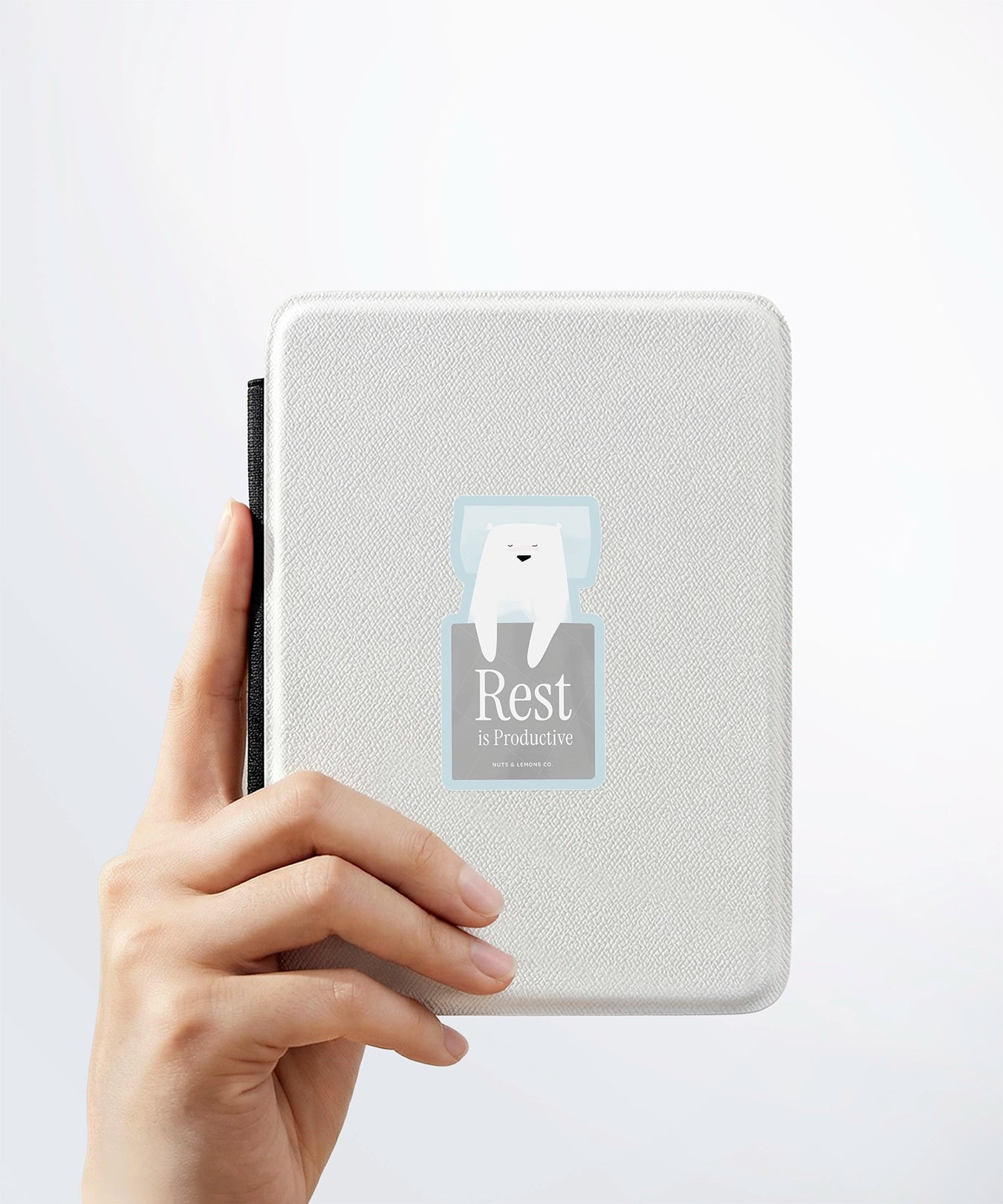 A hand holding a white kindle cover with a Nuts & Lemons Co. diecut sticker on it featuring a pretzel with the phrase “Baked with a Plot Twist”