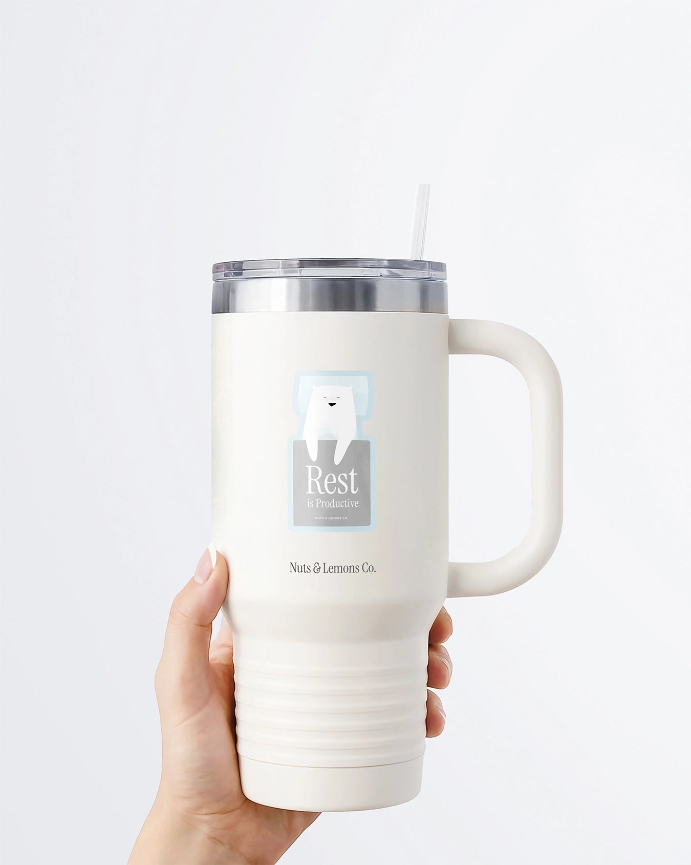 Hand holding a tumbler displaying Nuts & Lemons Co. diecut sticker featuring sleeping polar bear with the phrase “rest is productive”