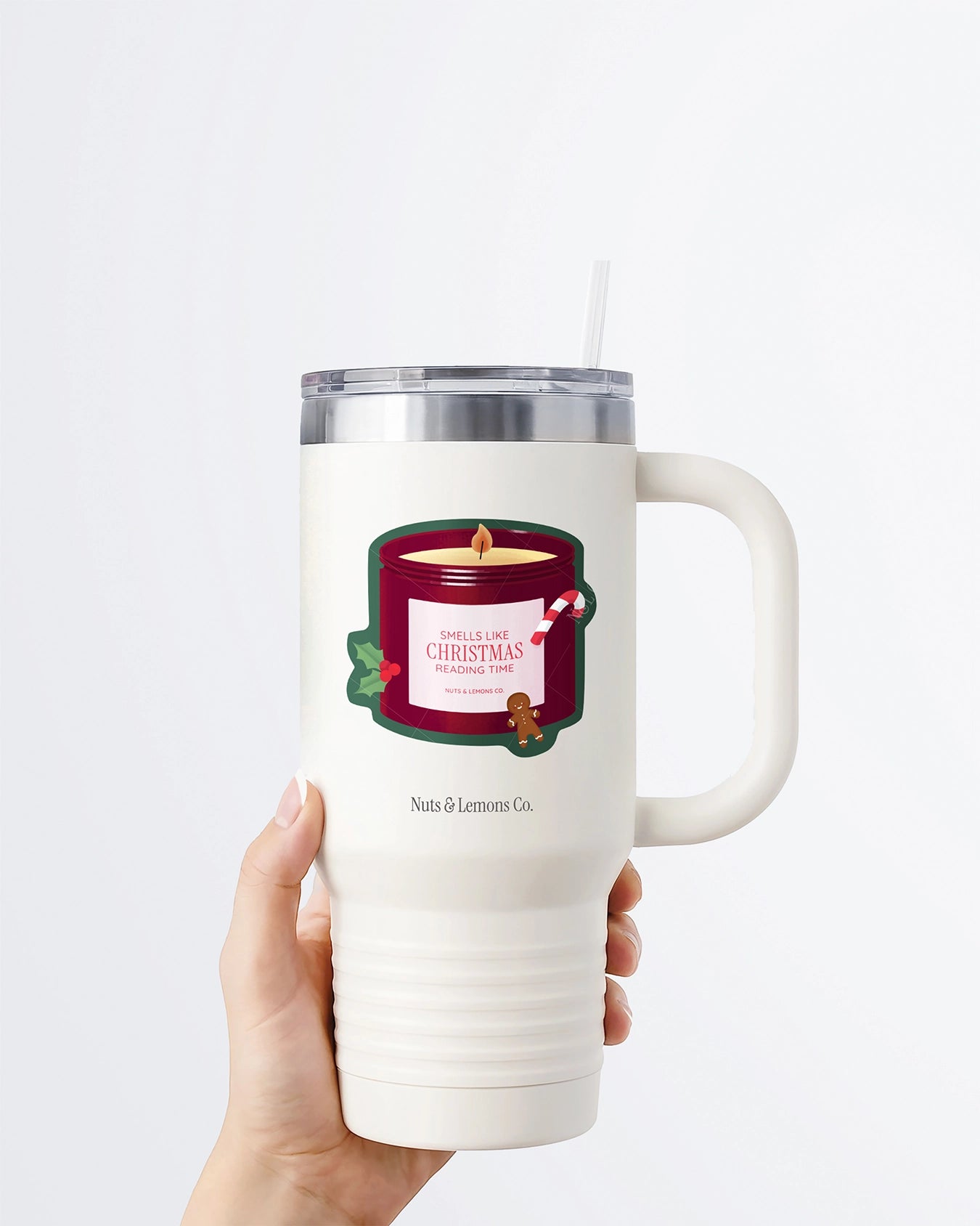 Hand holding a tumbler displaying Nuts & Lemons Co. diecut sticker featuring a Christmas candle with candy cane, gingerbread and a label with the phrase “smells like Christmas reading time” 