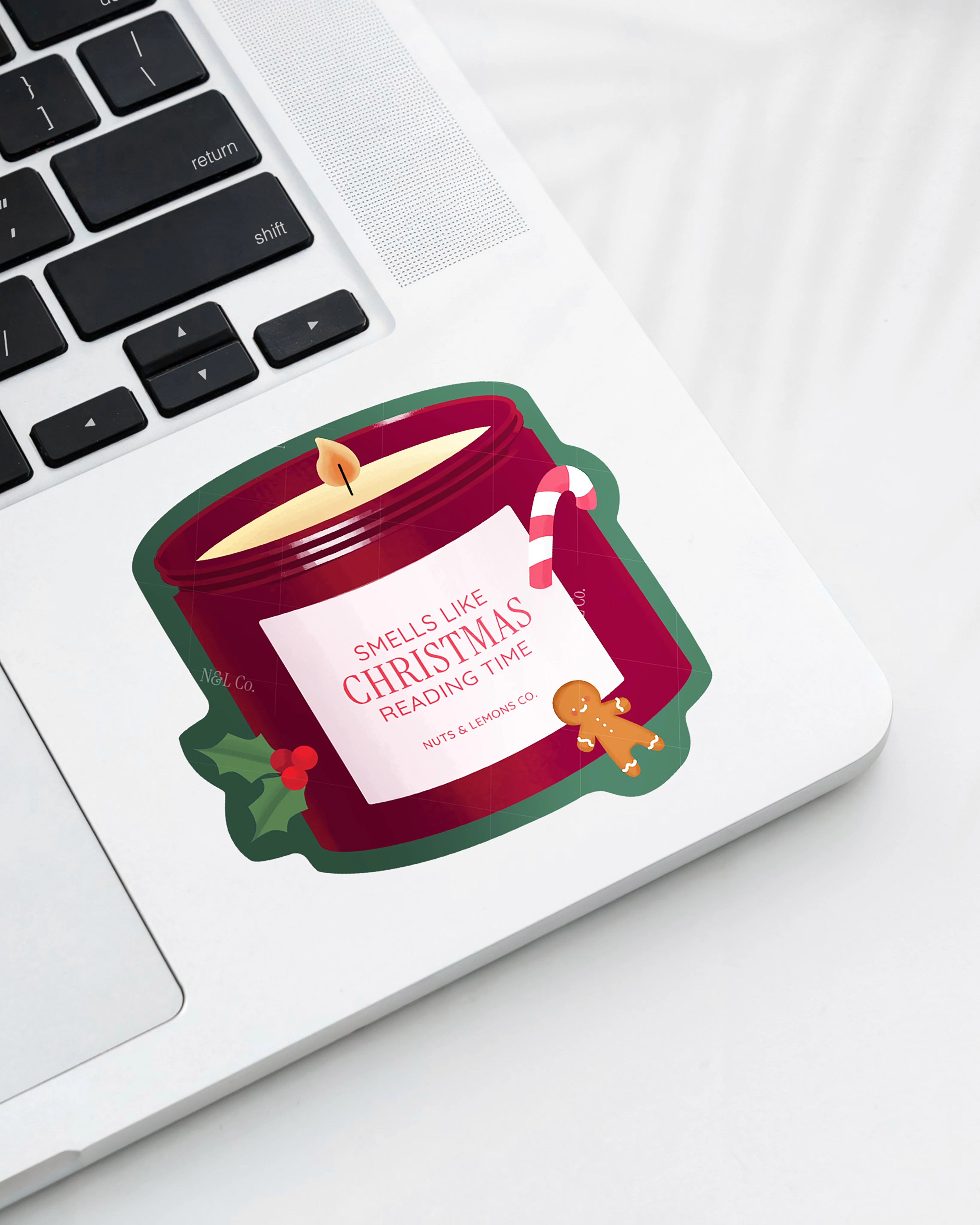 Laptop displaying a Nuts & Lemons Co. diecut sticker featuring  a Christmas candle with candy cane, gingerbread and a label with the phrase “smells like Christmas reading time”
