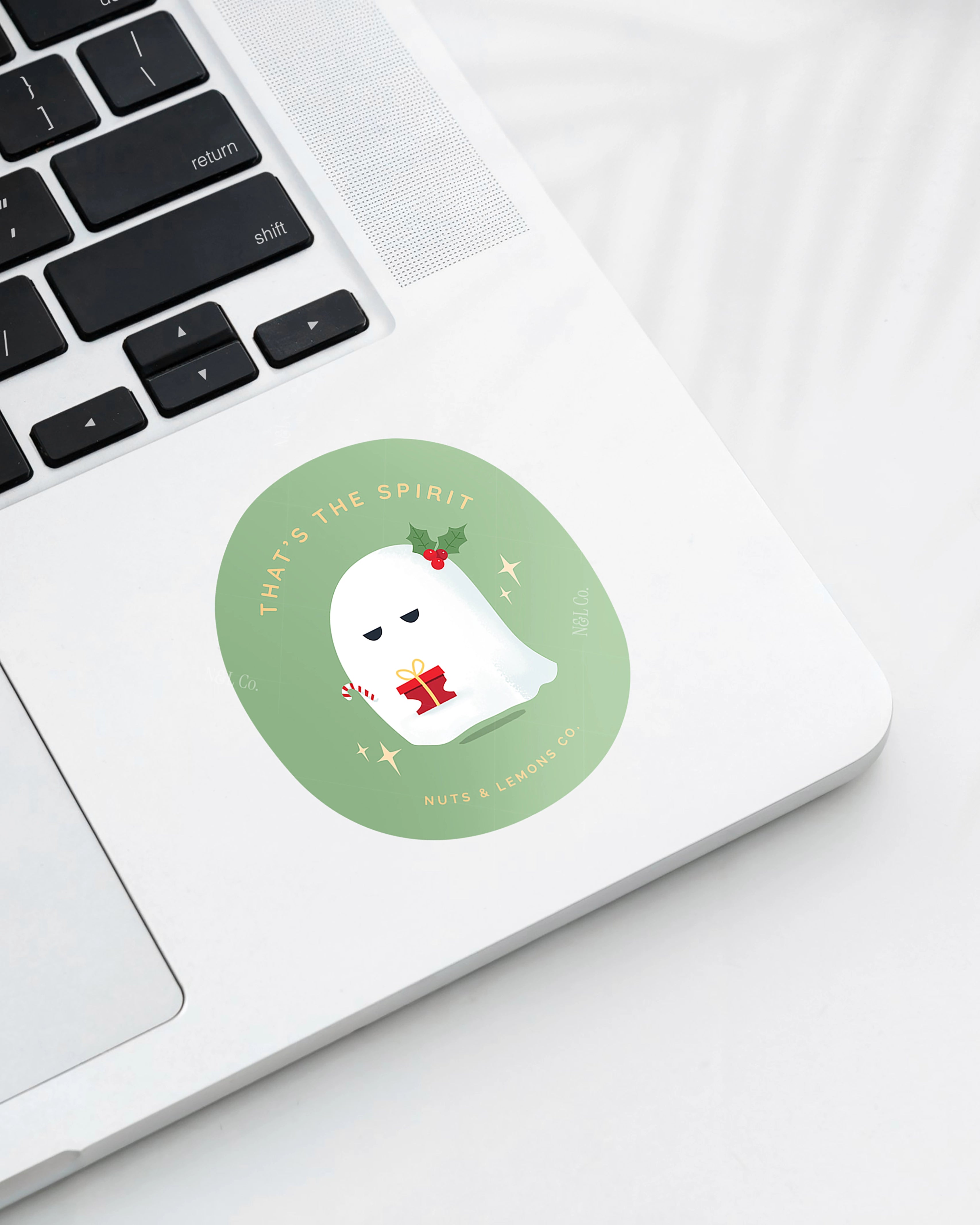 Laptop displaying a Nuts & Lemons Co. diecut sticker featuring  a cute pouting and grumpy ghostie  with a Christmas present with the phrase “that’s the spirit”