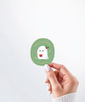 Hand holding a Nuts & Lemons Co. diecut sticker featuring a cute pouting and grumpy ghostie  with a Christmas present with the phrase “that’s the spirit”