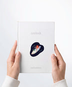 A pair of hands holding a white notebook with a Nuts & Lemons Co. diecut sticker on it featuring an ufo with an alien and octopus with the phrase “Two Peas on a Pod”