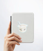 A hand holding a white kindle cover with a Nuts & Lemons Co. diecut sticker on it featuring a yogurt cup with the phrase “Yogurt Has More Culture”