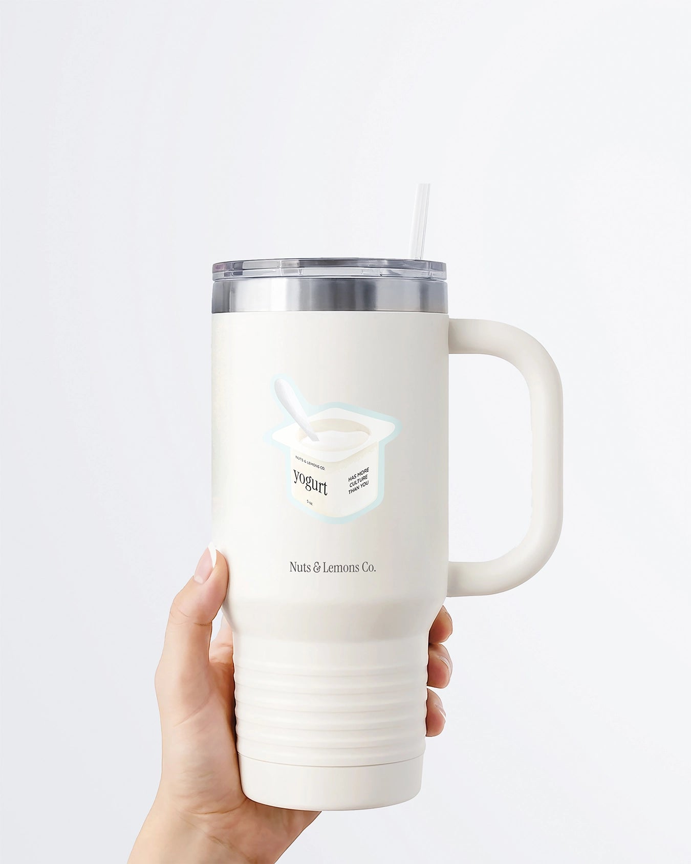 A hand holding a white tumbler with a Nuts & Lemons Co. diecut sticker on it featuring a yogurt cup with the phrase “Yogurt Has More Culture”