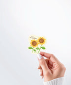 Hand holding a Nuts & Lemons Co. diecut sticker featuring a two sunflowers with the phrase “You Are My Sunshine”