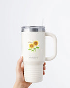 A hand holding a white tumbler with a Nuts & Lemons Co. diecut sticker on it featuring a two sunflowers with the phrase “You Are My Sunshine”