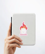 A hand holding a white kindle cover with a Nuts & Lemons Co. diecut sticker on it featuring a marshmallow on fire with the phrase “You’re on Fire”