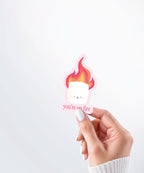 Hand holding a Nuts & Lemons Co. diecut sticker featuring a marshmallow on fire with the phrase “you’re on fire”