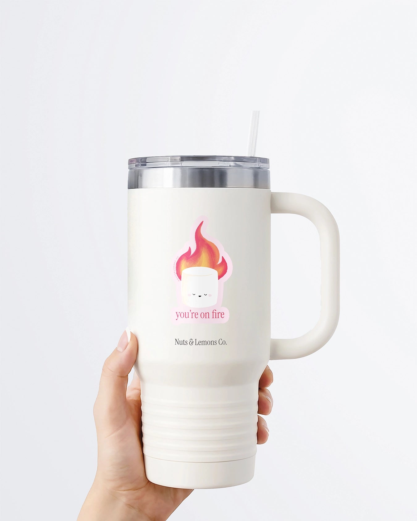 Hand holding a tumbler displaying Nuts & Lemons Co. diecut sticker featuring a marshmallow on fire with the phrase “you’re on fire”